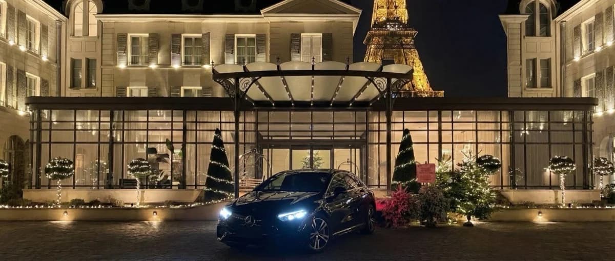 Voiture Mercedes chauffeur privé devant un hôtel de luxe parisien avec la Tour Eiffel illuminée de nuit